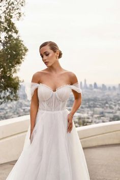 a woman in a white wedding dress standing on top of a hill with her hands on her hips