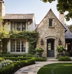 a stone house with hedges and bushes around the front door is surrounded by greenery