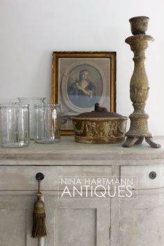 an antique dresser with glass jars and a painting on the wall next to it,