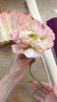 a person is holding a pink flower in their hand next to a piece of wood