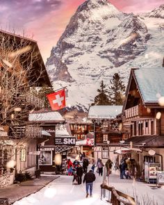 people are walking down the street in front of some buildings with mountains in the background