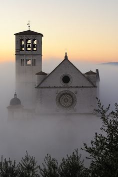 the church is surrounded by fog and low light in the morning hours, as it sits on top of a hill