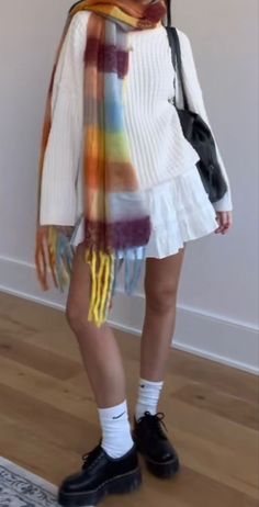 This outfit features a white pleated mini skirt paired with a loose-fitting, long-sleeved white sweater. The look is accessorized with a multicolored striped scarf draped over the shoulders, adding a pop of autumnal hues. The ensemble is completed with classic black platform shoes, white crew socks, and a small black shoulder bag, creating a stylish blend of comfort and vibrant seasonal flair.  fashion outfit ideas women fashion fall outfits fall aesthetic  #fashion #girlyoutfit #fall #autumn #falloutfits #fallgirlyoutfit #dresstoimpress #chicdresstoimpress #dresstoimpresscoronation #dresstoimpressregencyera #amusementparkdresstoimpress #datenightdresstoimpress #outfitsforfall #outfitinspocasual #fallvibes #dresstoimpresscodes Cold Picnic Outfit, White Mini Skirt Outfit, Fall Aesthetic Fashion, Platform Shoes White, White Pleated Mini Skirt, White Crew Socks, Outfits Fall Aesthetic, Skirt Outfit Fall, White Skirt Outfits