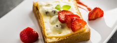 a piece of bread topped with fruit on top of a white plate next to strawberries