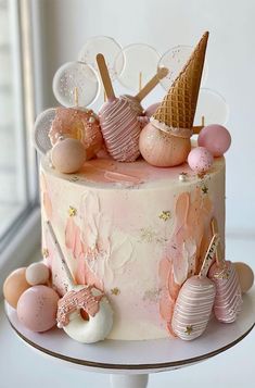 a pink and white cake with ice cream cones on top, surrounded by other decorations