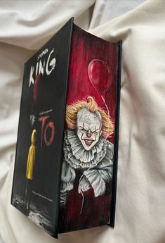 an open book with a drawing of a clown on the cover and a painting of a person holding a balloon