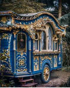 an ornate blue and gold carriage is parked in the woods near some trees with its doors open