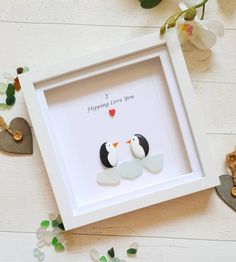 two penguins in a white frame with hearts and flowers on the table next to it