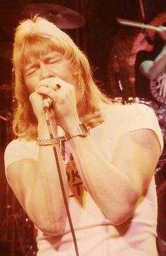 a man with long hair holding a microphone in front of his face while standing on stage