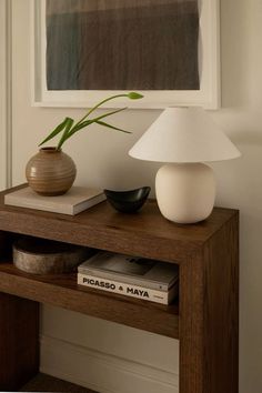 a table with a lamp, vase and books on it in front of a painting