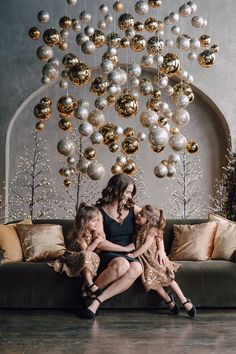 a woman and two children sitting on a couch in front of a christmas tree with ornaments