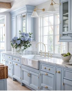 a kitchen with blue cabinets and white marble counter tops, gold pulls on the faucets