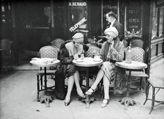 two women sitting at an outdoor table talking on their cell phones in front of a store