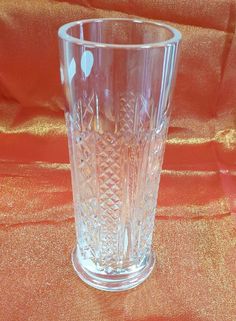 a clear glass vase sitting on top of a red cloth covered table with an orange fabric behind it