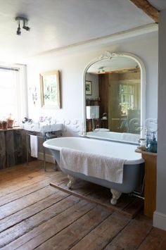 an old fashioned bathtub is in the middle of a wood floored bathroom with a large mirror on the wall