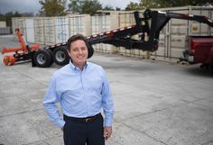 a man standing in front of a truck with cargo on it's trailer behind him