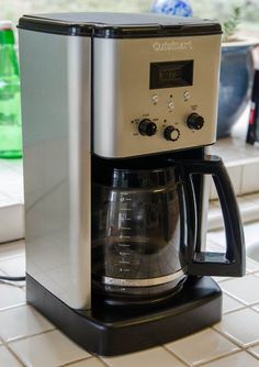 a silver and black coffee maker sitting on top of a white tiled kitchen countertop