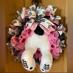 a teddy bear wreath is hanging on the front door with pink and black ribbon around it