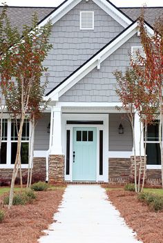 a blue front door and some trees in front of a gray house with white trim