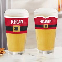 two glasses with beer and pretzels sitting on a counter top next to each other