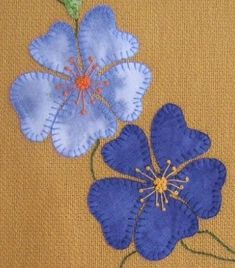 two blue flowers with green stems on a tan background are embroidered onto the side of a piece of fabric