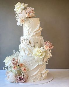 a three tiered wedding cake with flowers on the side and initials on the top