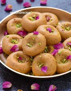 some food is in a bowl with petals on the table and pink flowers around it