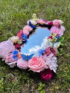 a heart shaped mirror with pink and blue flowers on the grass next to it is a sky reflection