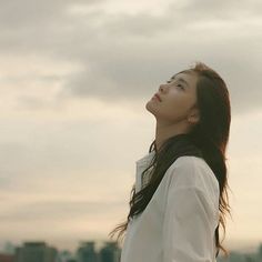 a woman looking up at the sky with buildings in the background