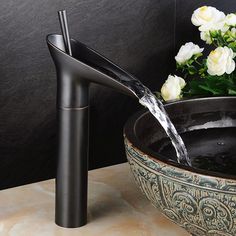 a black faucet is pouring water into a bowl with white flowers in the background