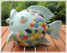 a colorful ceramic fish sitting on top of a wooden table in front of some trees