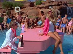 a group of people in swimsuits sitting around a pool with a pink piano