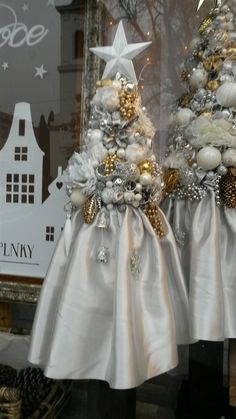 two white christmas trees in front of a window with gold and silver decorations on them