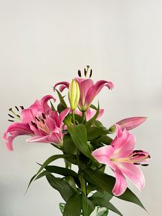 a vase filled with pink lilies on top of a wooden table next to a white wall