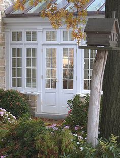 a white door and window in front of a house with flowers on the ground next to it