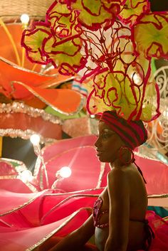 a woman sitting on the ground in front of many colorful umbrellas and flowers hanging from her head