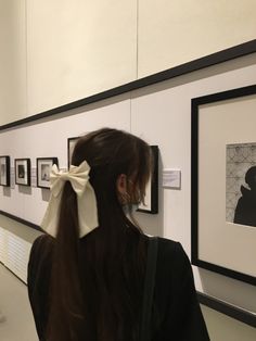 a woman with a bow in her hair looking at pictures on the wall