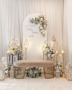 a white and gold wedding set up with flowers on the wall, candles, and a bench