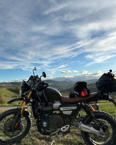 a motorcycle parked on top of a lush green hillside under a blue sky with clouds