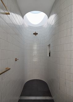 an empty white tiled bathroom with skylight above