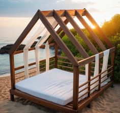 a bed made out of wood and white sheets on top of sand at the beach