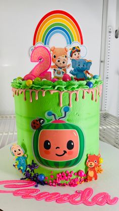 a birthday cake decorated with cartoon characters and rainbows on the top, sitting on a table