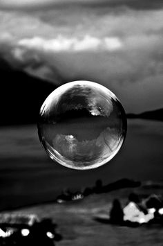 a woman is blowing bubbles in front of the water and mountains with her hand up to her face