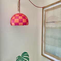 a pink and orange lamp hanging from the ceiling next to a green potted plant