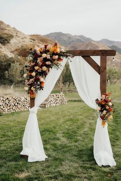 an outdoor wedding ceremony setup with white drapes and orange flowers on the back drop cloth