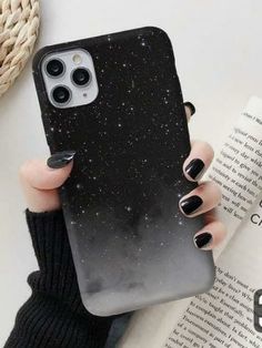 a woman holding up her phone case with black and white stars on the back, in front of an open book