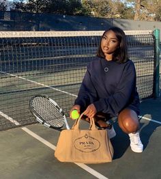 a woman sitting on the ground with a bag and tennis racket in front of her