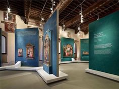 several paintings on display in a museum with blue walls and white pedestals, suspended from the ceiling