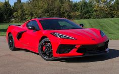 a red sports car parked in a parking lot next to some grass and trees on a sunny day