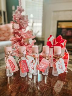 five small bottles with pink and white labels on them sitting on a table next to a christmas tree